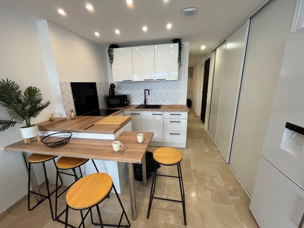 Une cuisine moderne avec des meubles blancs, un îlot central en bois et des tabourets de bar.