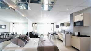 A modern hotel room with a large bed, a kitchenette, and a dining area.