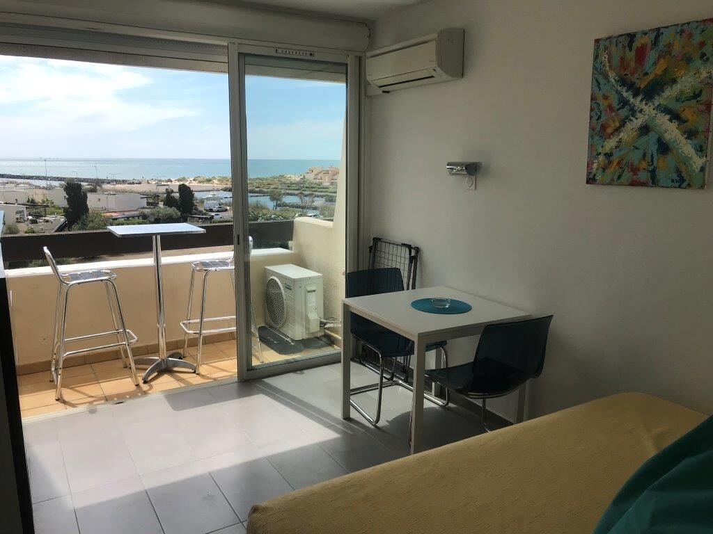 A balcony with a view of the sea, a dining table with chairs, and an air conditioning unit.