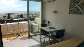 A balcony with a view of the sea, a dining table with chairs, and an air conditioning unit.