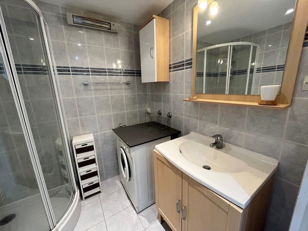 Een kleine badkamer met douche, wastafel, spiegel en een kastje.
