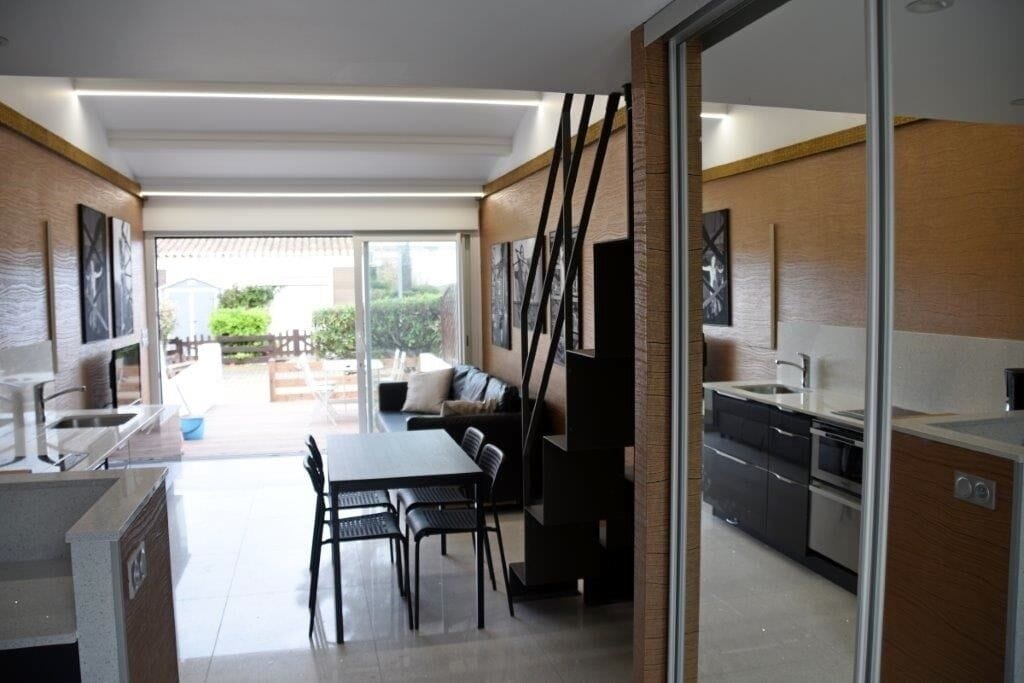A modern kitchen with a dining area, large windows, and a view of the outdoors.
