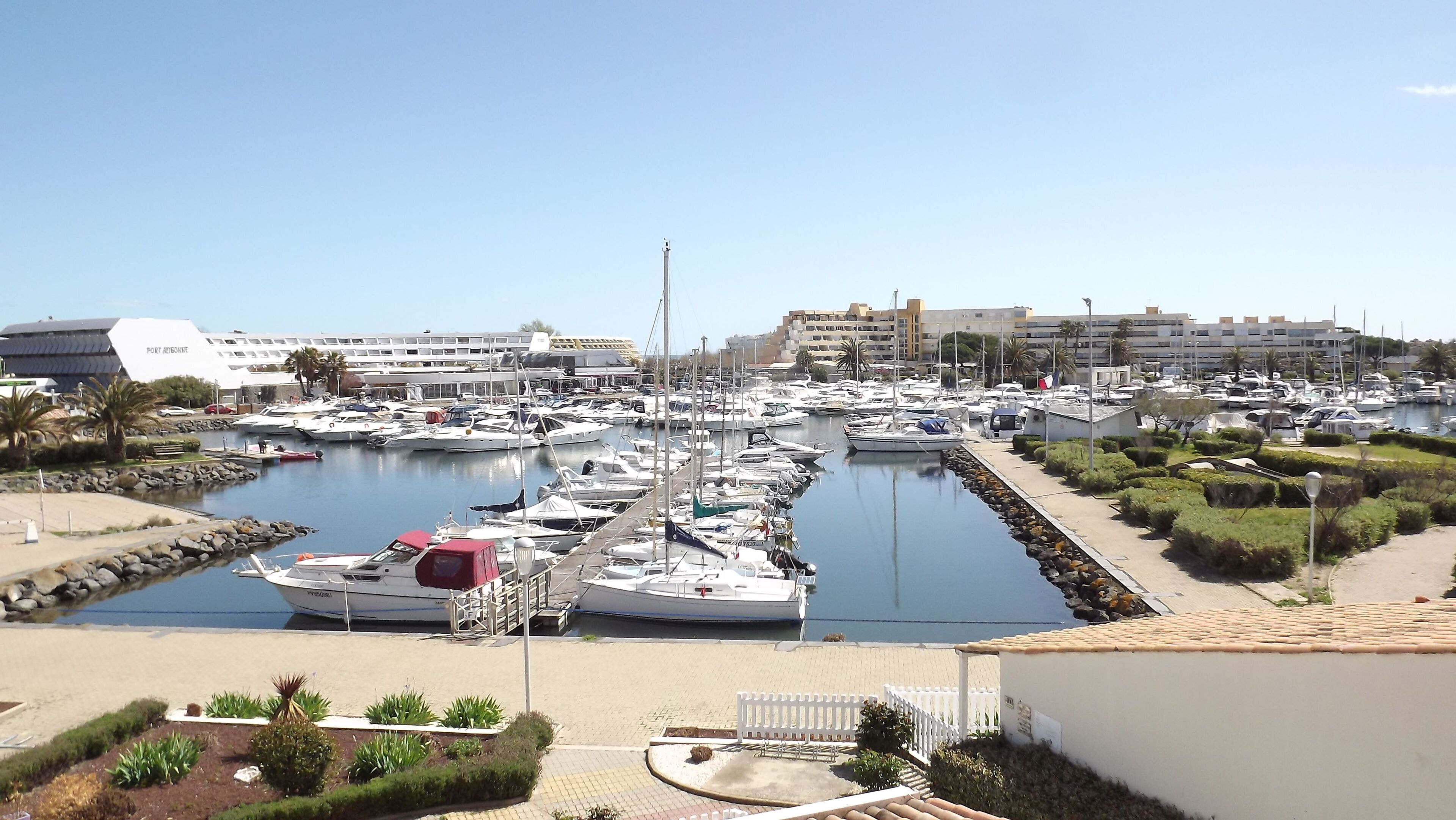 A marina with numerous boats docked, a building labeled 'PORT AERONORTE,' and a clear sky.