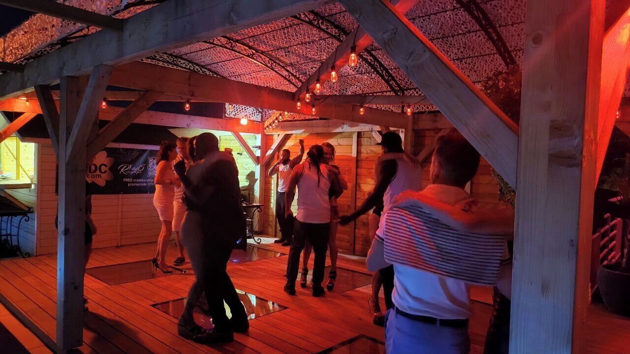 A wooden deck with people dancing, a covered area with a patterned ceiling, and a sign with 'Free membership' visible.