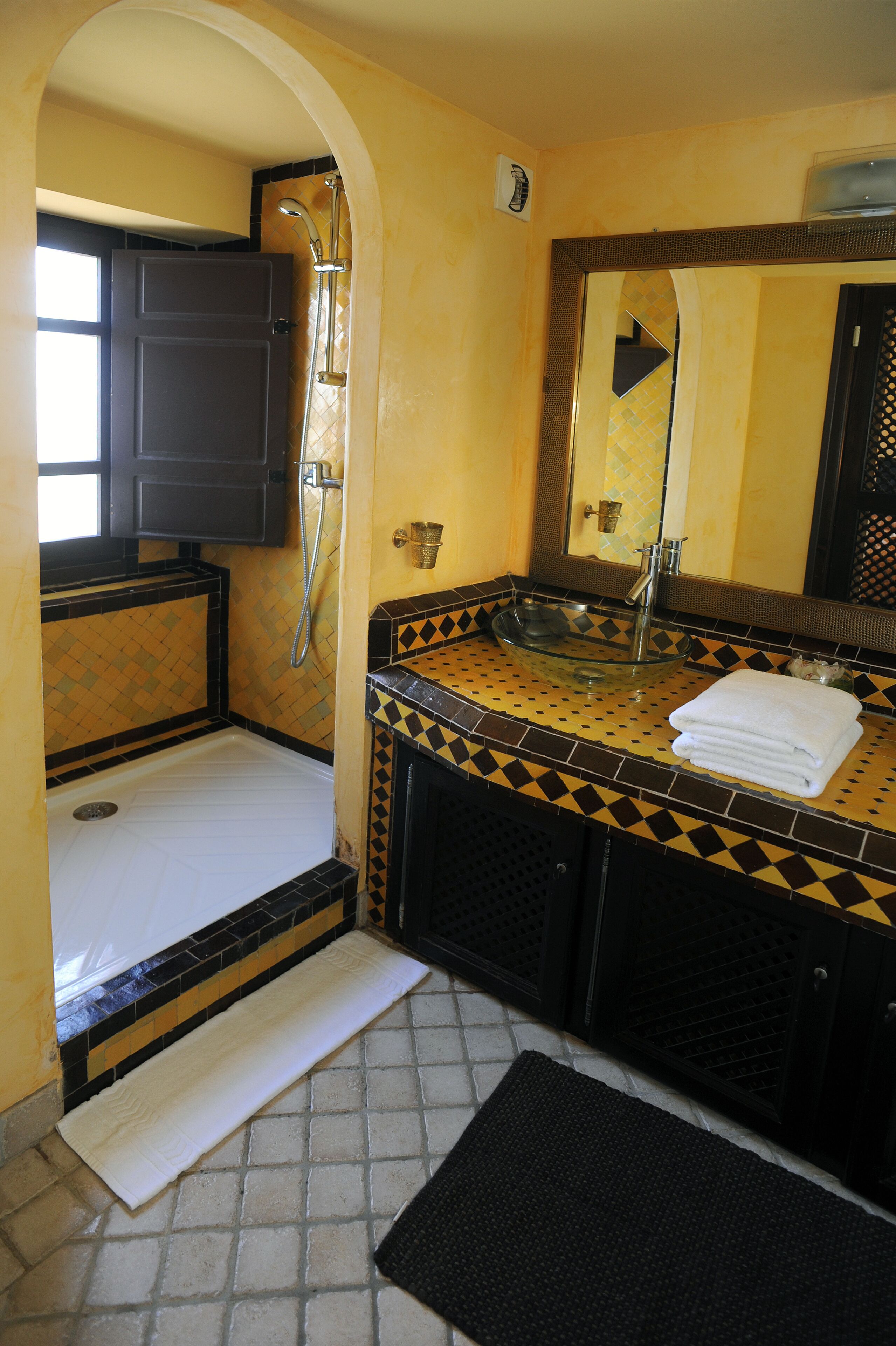 A compact bathroom with a shower, a sink with a glass basin, and a mirror above the sink.