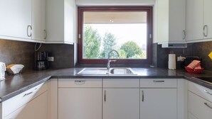 A modern kitchen with white cabinets, a stainless steel sink, and a window with blinds. - Vacation home Haus am Deich in Reußenköge for up to 6 people (Reußenköge)