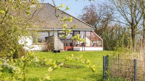 A house with a large glass window, a wooden deck, and a fenced yard. - Vacation home Haus am Deich in Reußenköge for up to 6 people (Reußenköge)