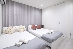 A hotel room with two beds, grey bedding, white pillows, and a striped wallpaper headboard. - Petanigeimasato (Osaka)