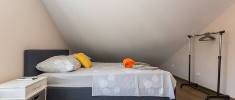A bedroom with a bed, pillows, a bedside table, a hanging rack, and a small rug.