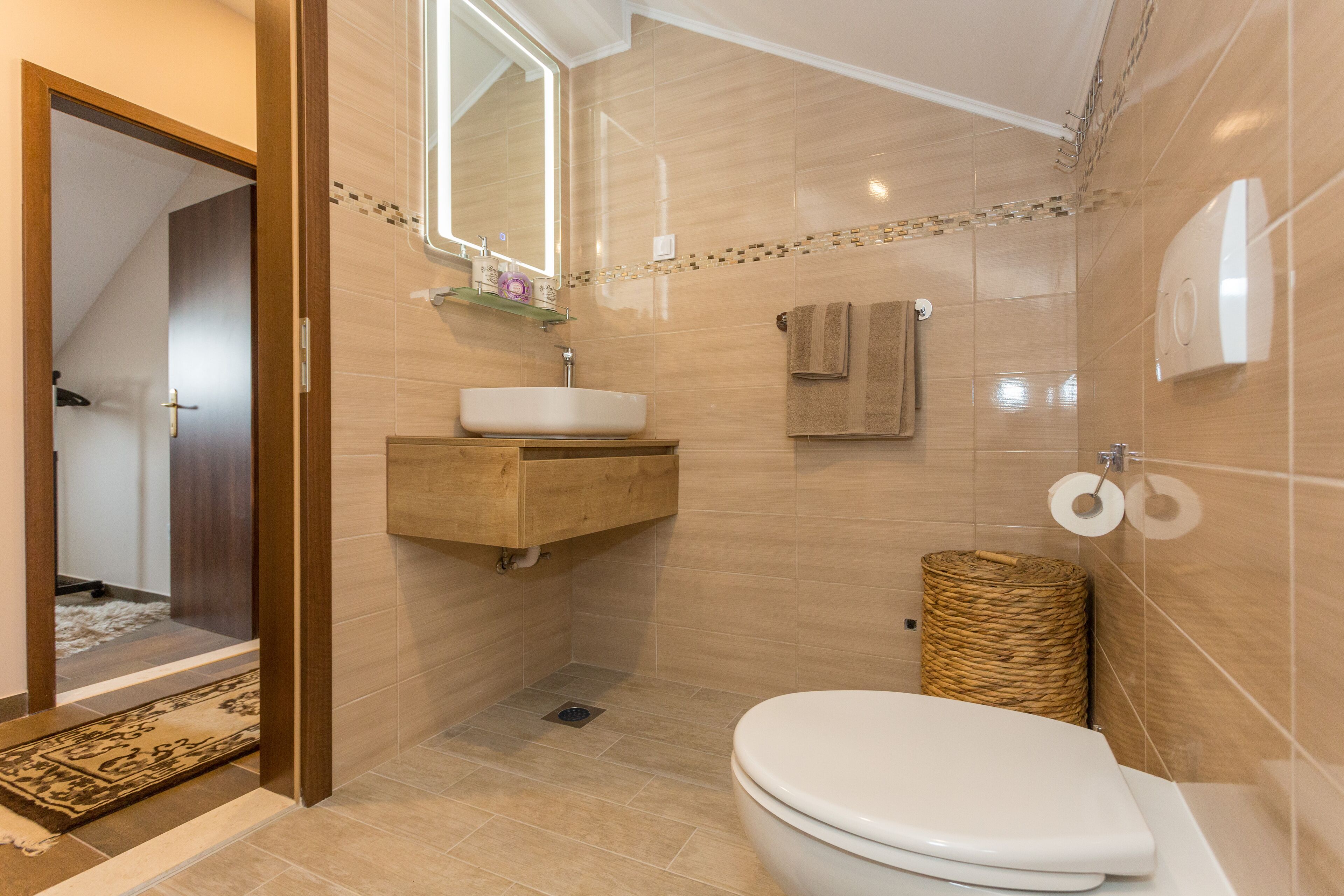 Een moderne badkamer met een houten wastafelmeubel, een witte wastafel, een toilet en een douchegedeelte.