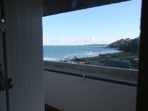 Vista desde una ventana sobre una zona costera con playa, muelle y edificios a lo lejos.