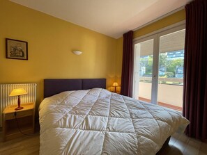 Habitación de hotel con cama, mesita de noche con lámpara, ventana con cortinas y radiador.
