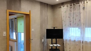 A room with a wooden table, a TV on a stand, and a door leading to another room.