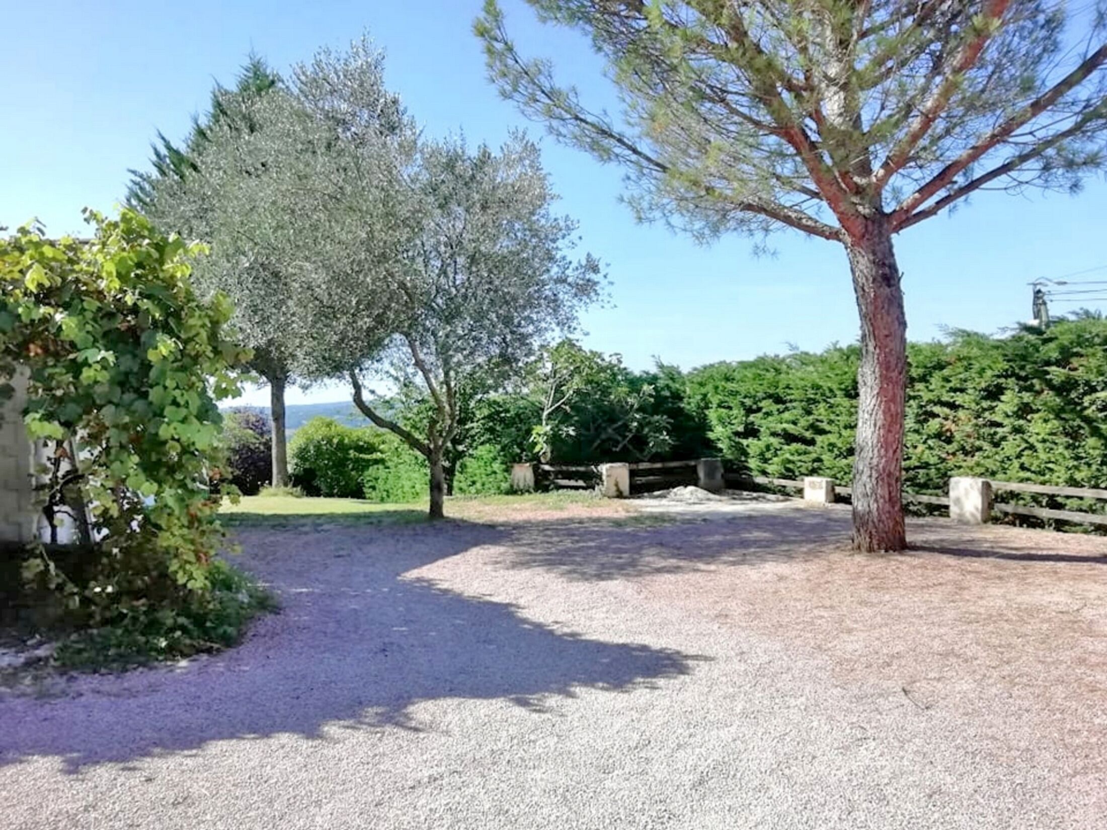 A gravel path leading to a wooden fence, surrounded by trees and greenery.