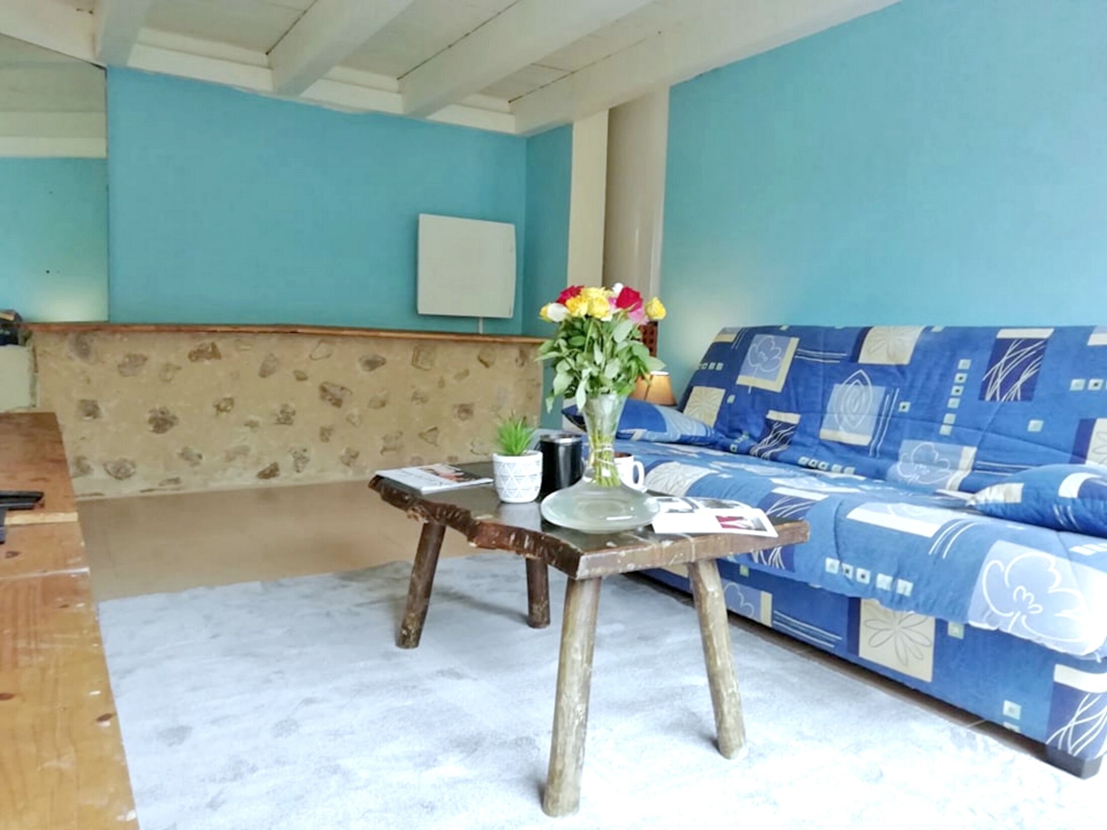 A room with a blue sofa, a wooden table with a vase of flowers, and a stone-patterned wall.