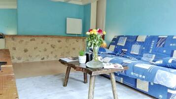 A room with a blue sofa, a wooden table with a vase of flowers, and a stone-patterned wall.
