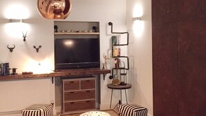 Moderni olohuone, jossa on suuri litteänäyttöinen televisio, puinen sohvapöytä, raidalliset koristetyynyt, punainen viltti ja ainutlaatuinen kattovalaisin.