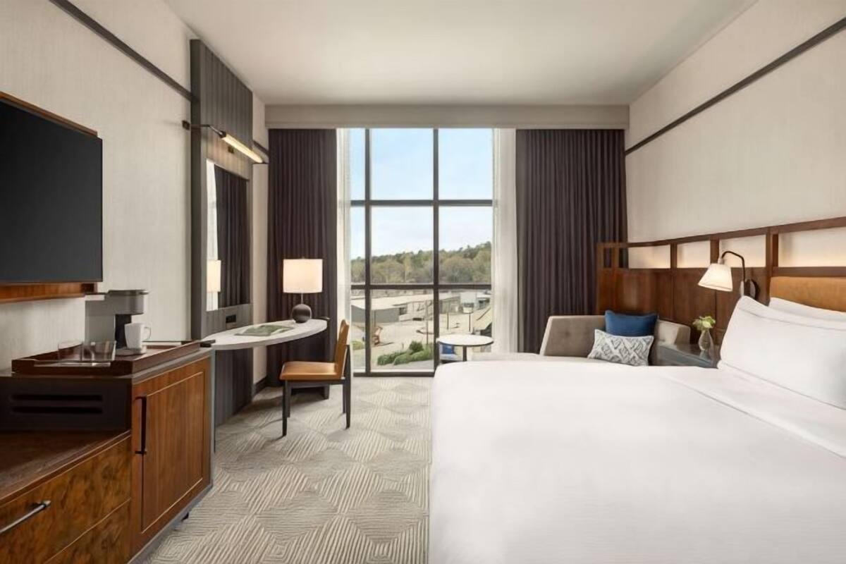 A hotel room with a bed, desk, chair, and a large window offering a view.