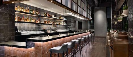 A modern bar area with a long counter, multiple shelves of bottles, and bar stools.