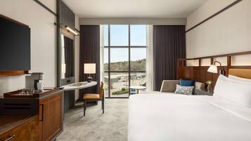 Habitación de hotel con una cama grande, un escritorio con silla, una mesita y un televisor.