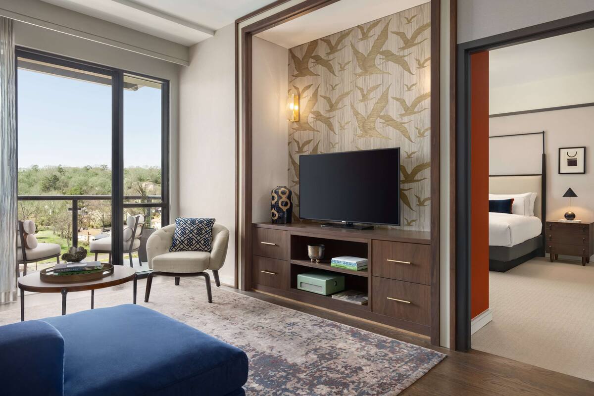 A modern hotel room with a large TV, comfortable seating, a balcony with a view, and a neatly organized entertainment area.
