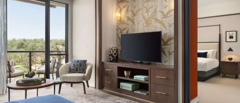 Habitación de hotel moderna con un televisor grande, asientos cómodos, un balcón con vistas y una zona de entretenimiento ordenada.