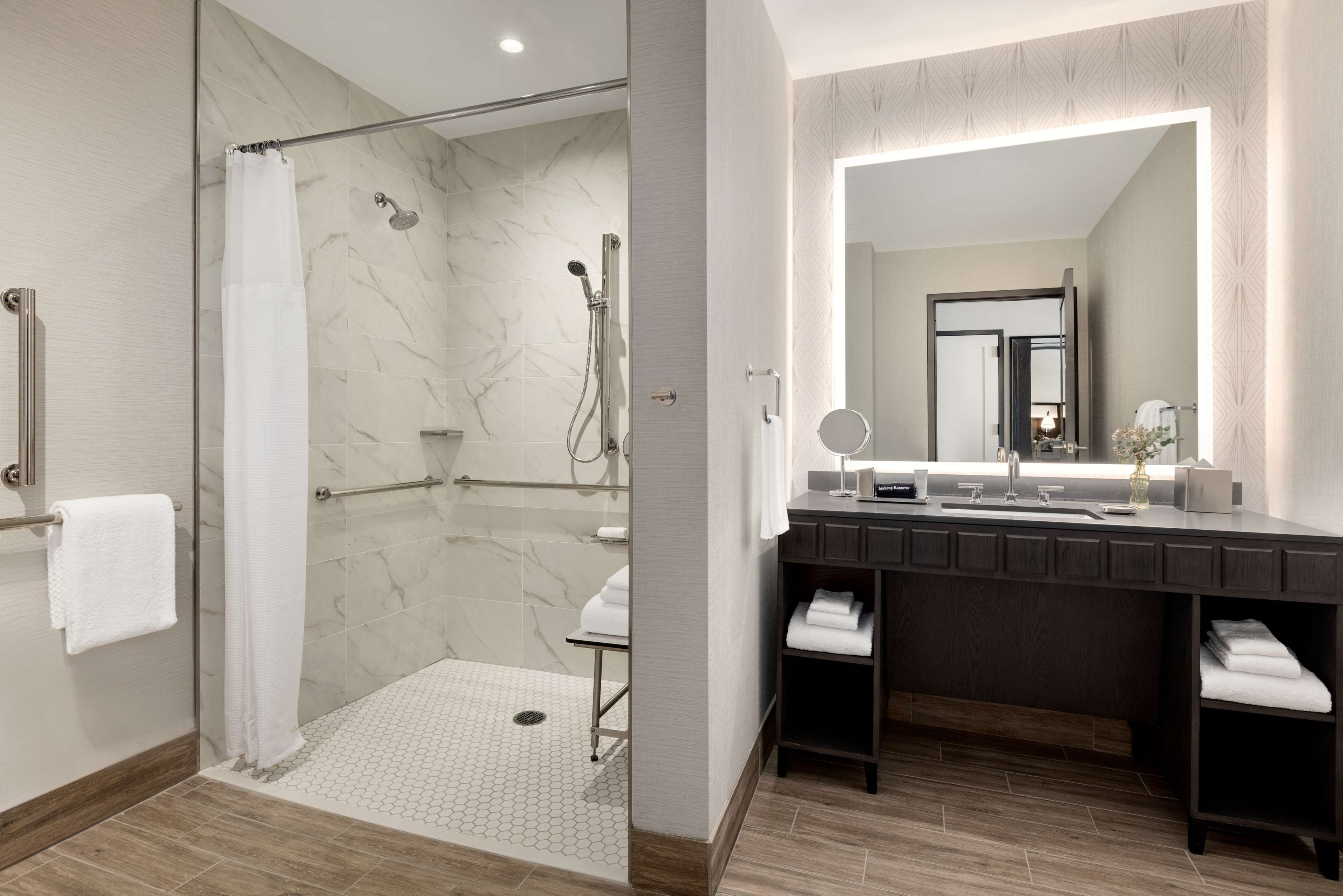Un baño moderno con cabina de ducha de vidrio, un espejo grande y un tocador de madera oscura.