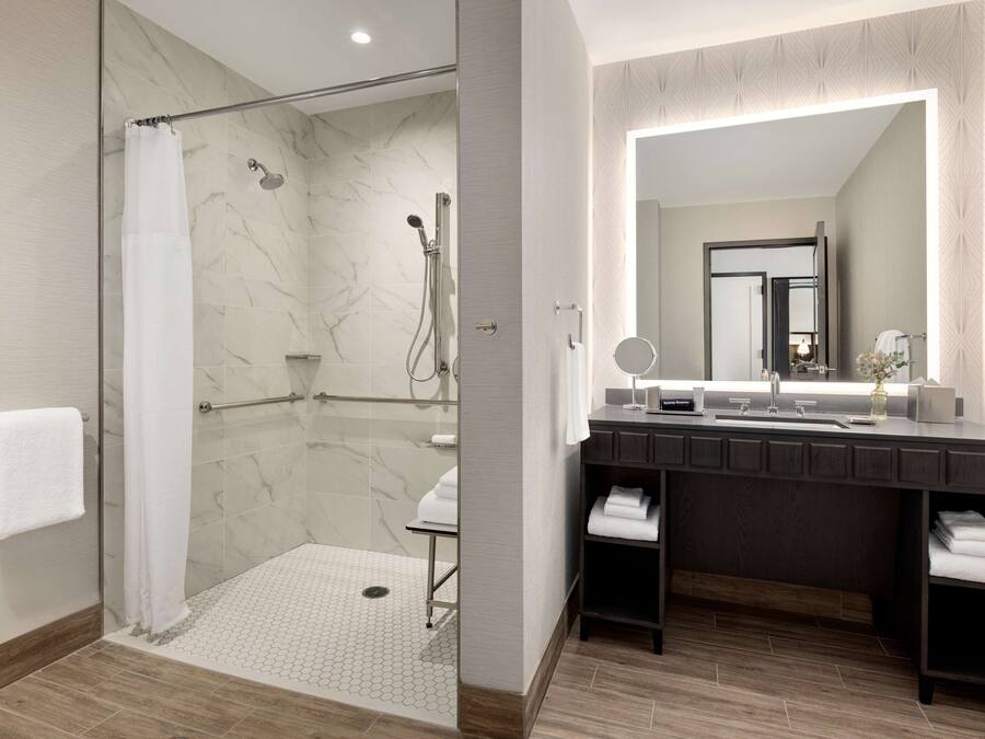 Un baño moderno con cabina de ducha de vidrio, un espejo grande y un tocador de madera oscura.