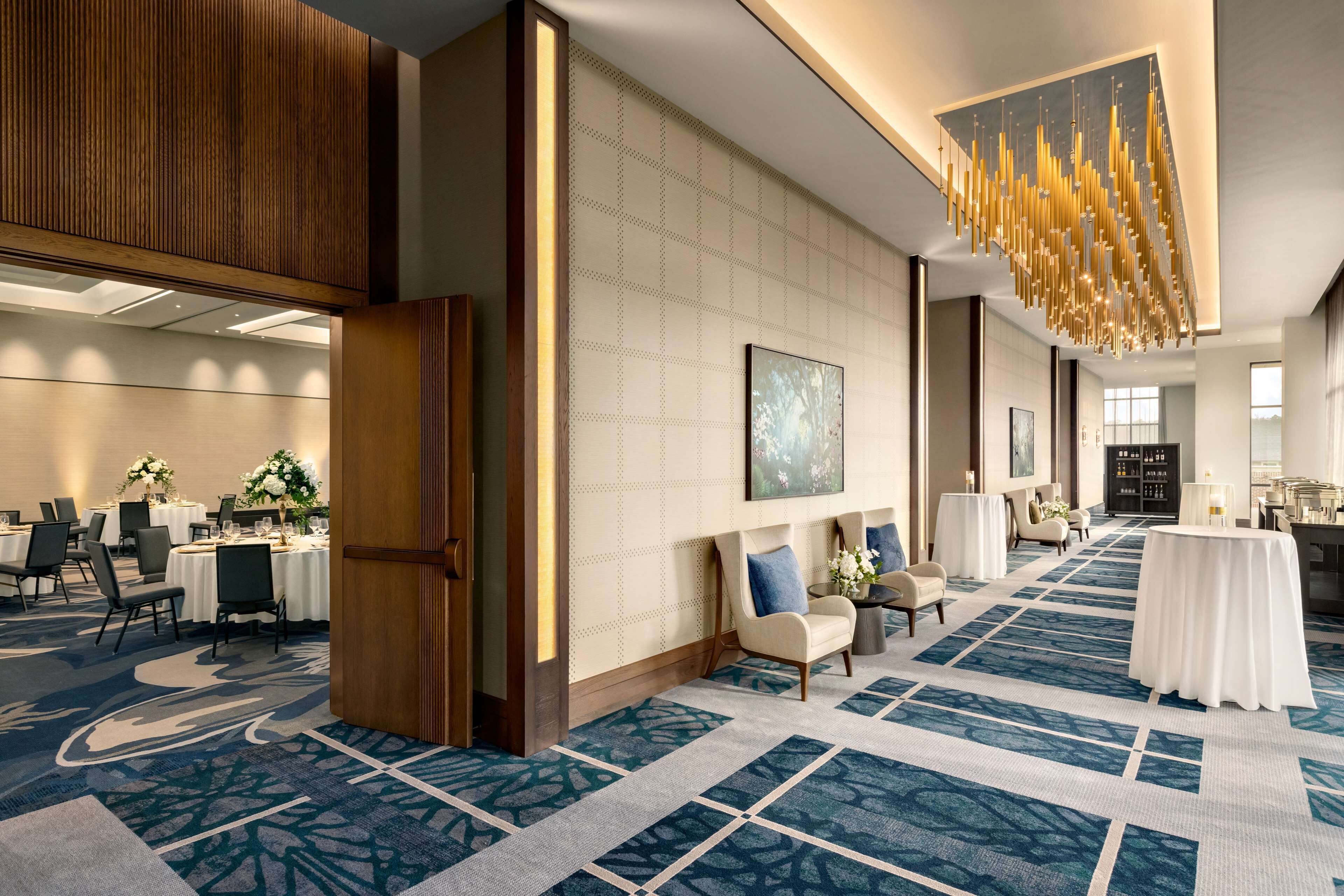A hotel lobby with a patterned carpet, a large chandelier, and a seating area with a table and chairs.