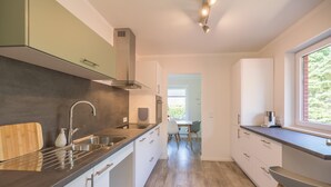 Een moderne keuken met een centraal eiland, roestvrijstalen apparatuur en uitzicht op de eetruimte.