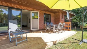 Een terras met een gele parasol, zitplaatsen buiten en een bakstenen gebouw met schuifpuien.
