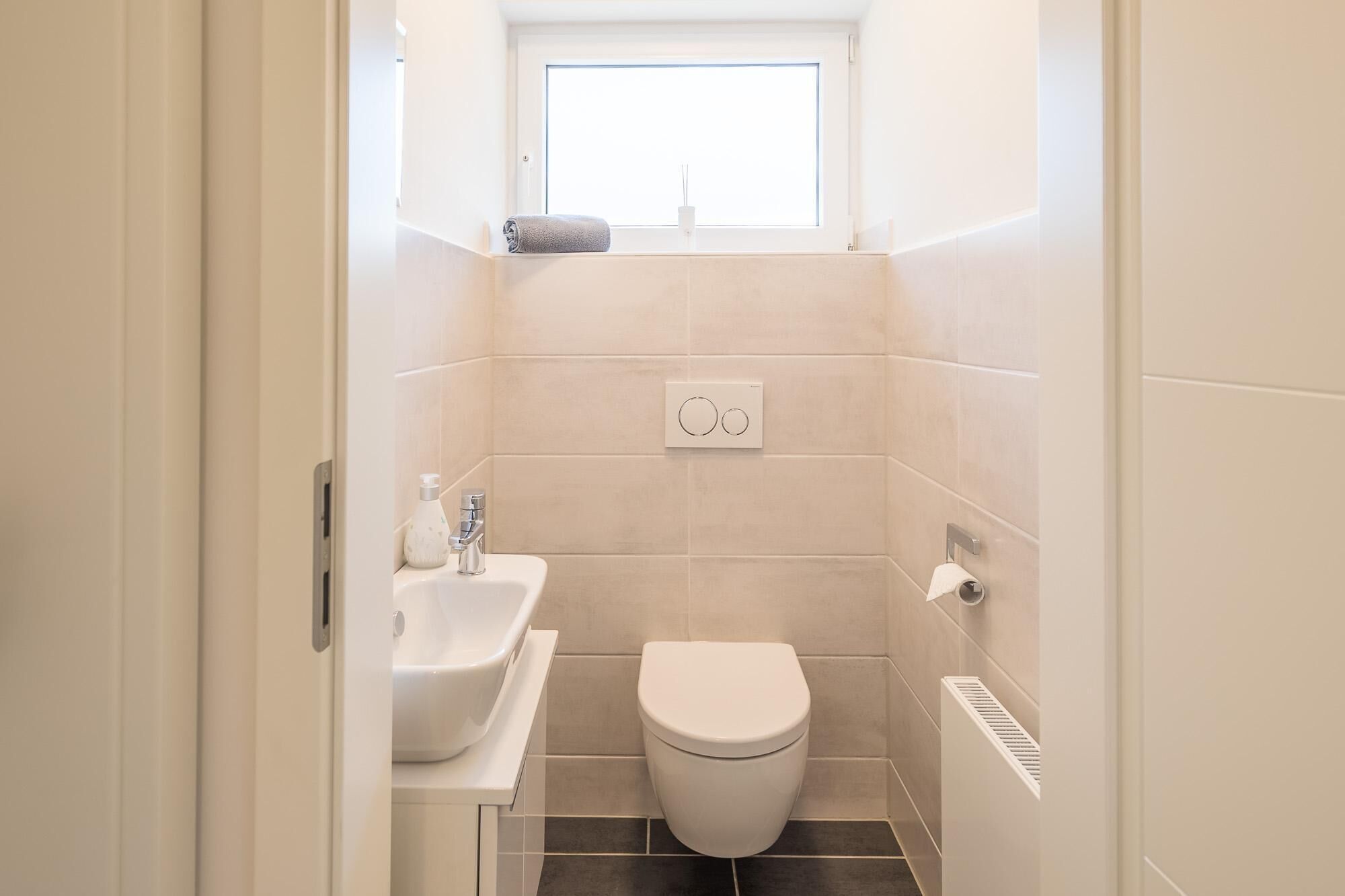 A small, modern bathroom with a toilet, sink, and window.