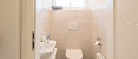 A small, modern bathroom with a toilet, sink, and window.