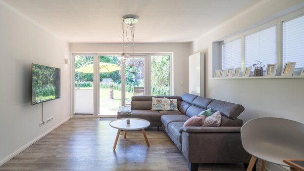 Een moderne woonkamer met een grijze bank, een ronde salontafel en een flatscreen televisie aan de muur.