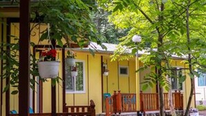 A yellow building with a wooden porch, a small staircase, and hanging flower baskets.