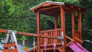 A wooden play structure with a slide, swings, and climbing holds.