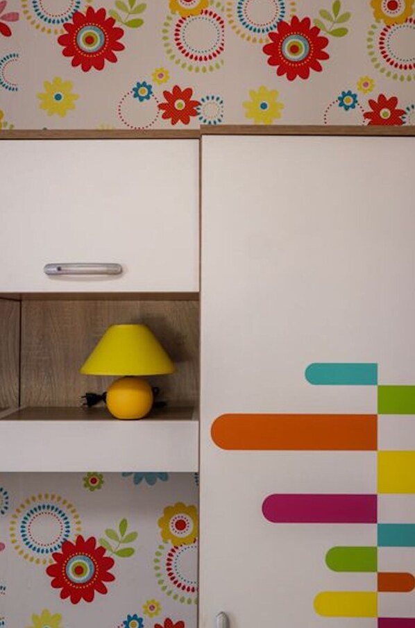 A room with a wooden cabinet, a yellow lamp, and a wall with colorful circular patterns. - Perfect place for 2 or 3 (Kamena)