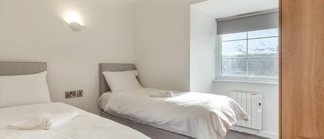 Un dormitorio con dos camas, una ventana con vistas y un radiador.