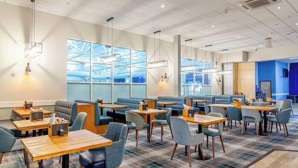 A modern hotel lobby with seating areas, tables, and large windows offering views of the sky and a building structure. - Apartment With Access to Pool, Spa & Soft Play (Ilfracombe)
