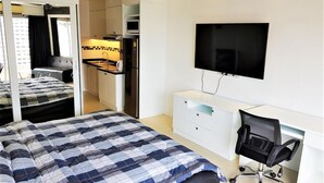A hotel room with a bed, a desk, a chair, a TV, and a kitchenette. - 11th Floor Studio at View Talay 1 (Pattaya)