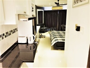 A compact hotel room with a kitchenette, a bed with a checkered bedspread, a black office chair, and a black desk with a chair. - 11th Floor Studio at View Talay 1 (Pattaya)