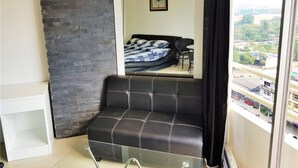 A modern living space with a black leather sofa, a glass coffee table, and a view of a cityscape through a large window. - 11th Floor Studio at View Talay 1 (Pattaya)