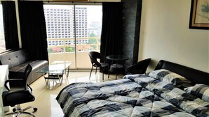 A modern hotel room with a large bed, a desk, a chair, and a balcony with a view of buildings. - 11th Floor Studio at View Talay 1 (Pattaya)