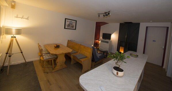 Un espacio habitable compacto con comedor, una pequeña kitchenette, televisor y una planta en maceta.