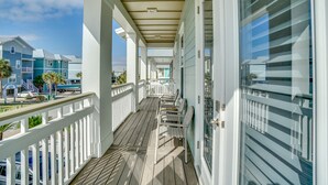 A covered wooden deck with white railings, a view of the ocean, and a building with a blue facade in the background. - Latitude Adjustment - 4 BR Luxury Gulf-Front, Pool, Sleeps 16 (Panama City Beach)