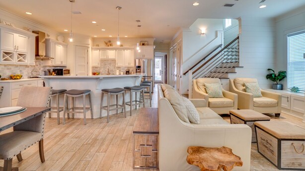A modern kitchen with white cabinetry, a central island with stools, and a staircase leading to an upper level. - Latitude Adjustment - 4 BR Luxury Gulf-Front, Pool, Sleeps 16 (Panama City Beach)