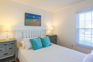 Een slaapkamer met een bed, twee nachtkastjes, een venster met jaloezieën en een schilderij aan de muur.