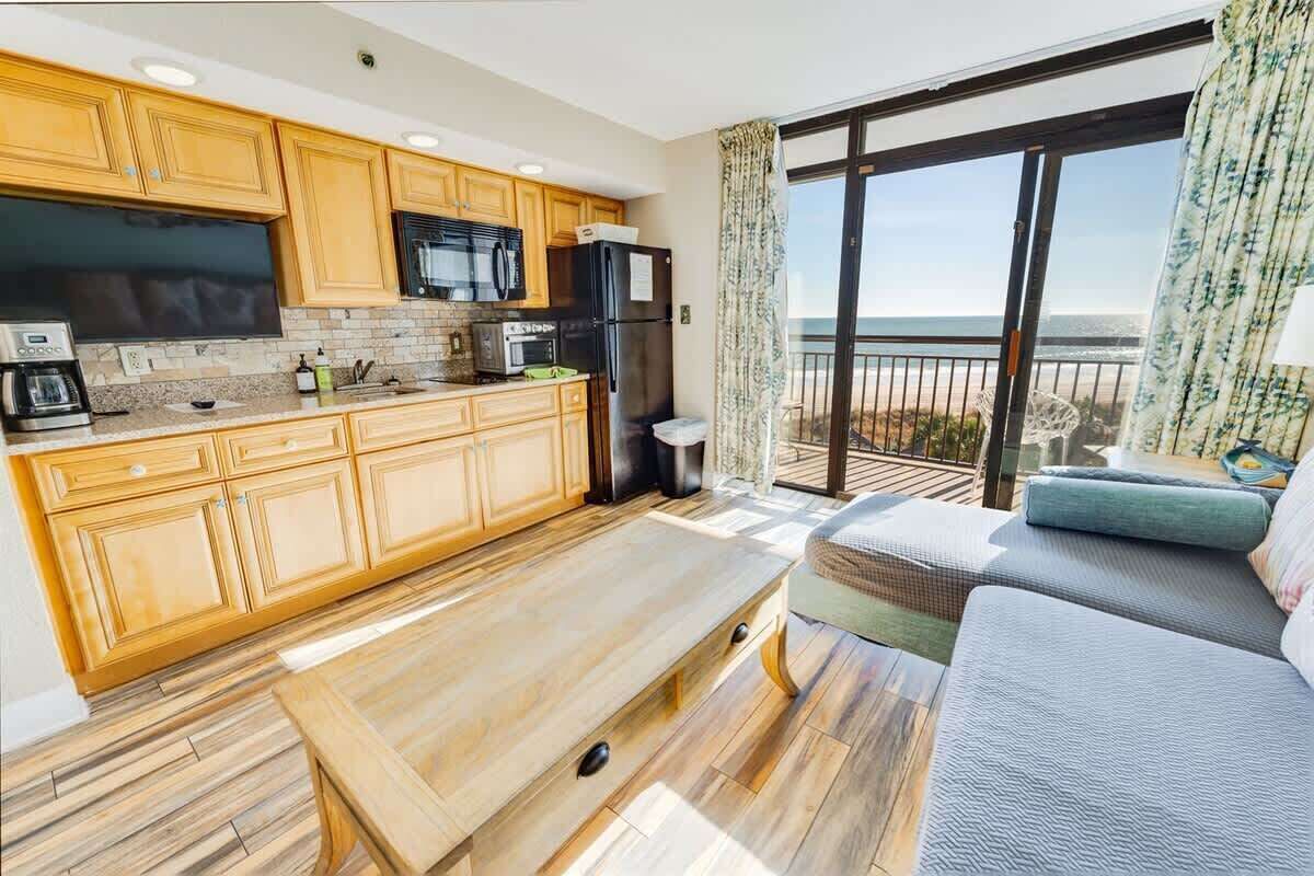 A modern kitchen with wooden cabinets, a black refrigerator, and a large window overlooking a balcony.