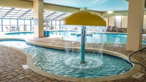 An indoor swimming pool with a central water feature, surrounded by lounge chairs and a tiled deck. - Oceanfront,Heated Pools,Views New, Penthouse Level (Myrtle Beach)