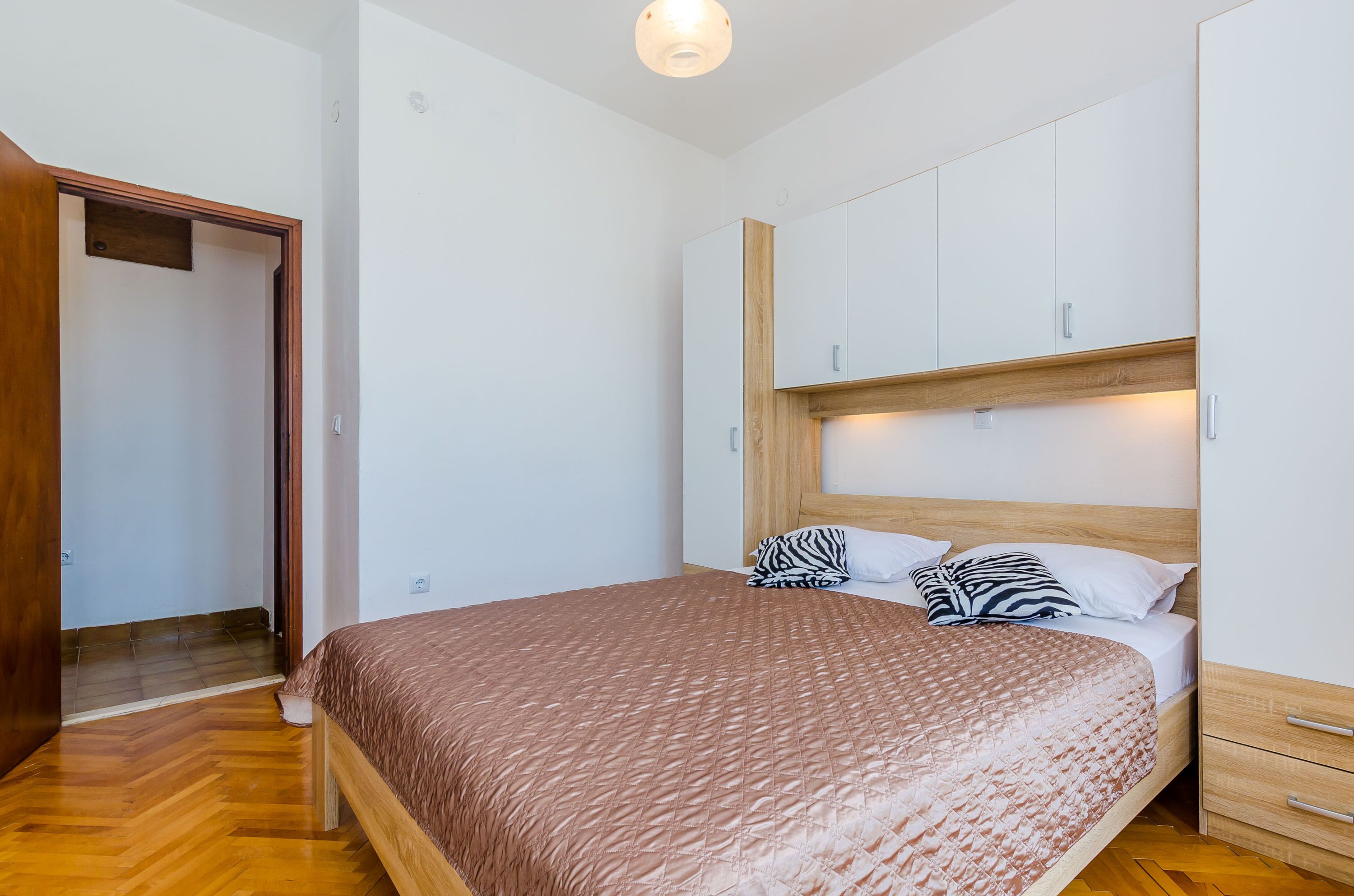 A bedroom with a wooden bed, white cabinets, and a wooden floor.